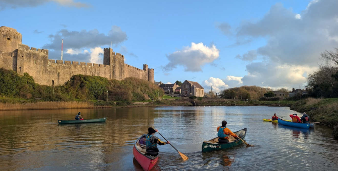 Four people in kayaks on a lake in front of a castle
