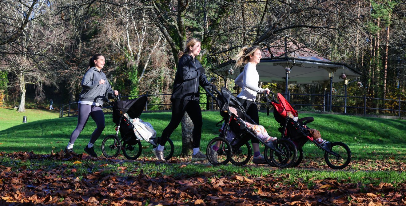 Three women with pushchairs run through a park