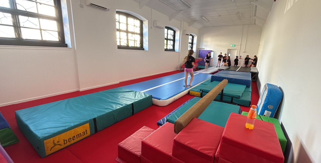 Children using inflatable gymnastics track and balance beam in an indoor training hall.
