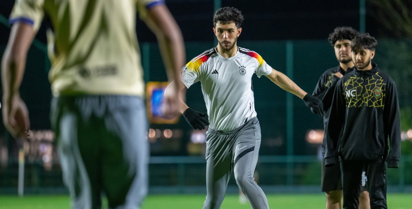Four men are on a football pitch, one is preparing to kick the ball