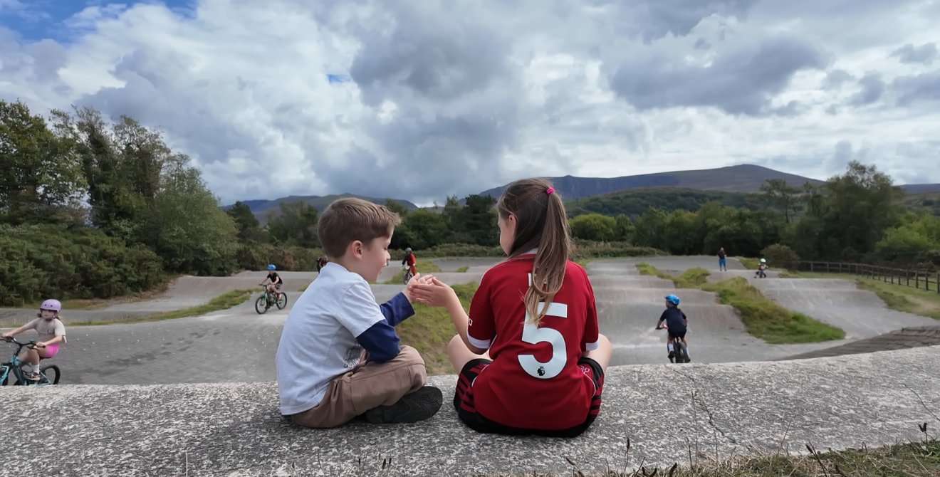 Two children sat in front of a bike track.