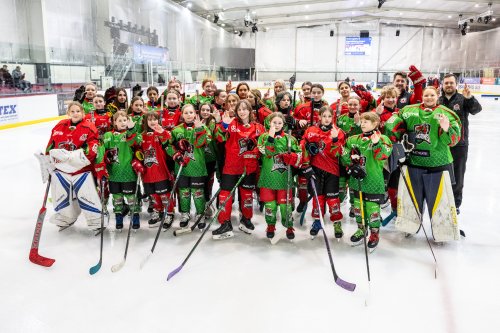 Group photo of the junior team in full kit on the ice rink, holding their hands up in the National Lottery crossed-finger pose.