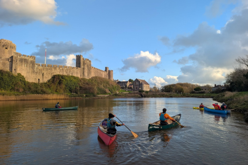 Four people in kayaks on a lake in front of a castle