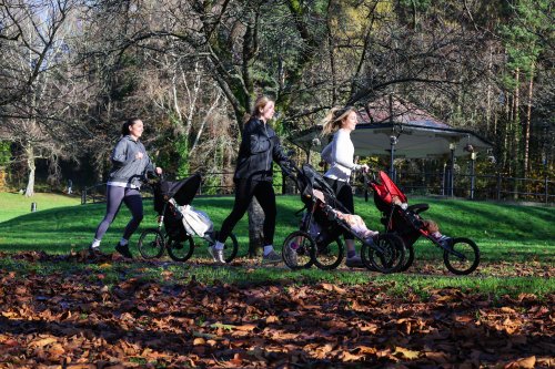 Three women with pushchairs run through a park