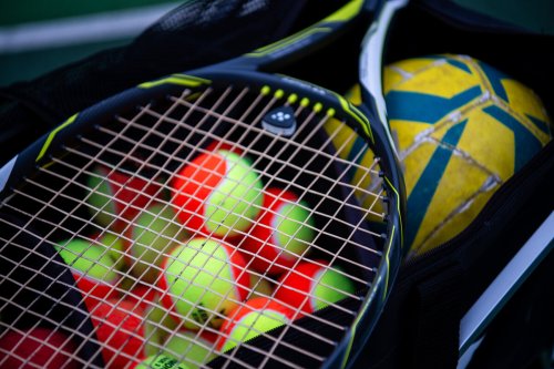 A tennis racket, tennis balls and a football in a kit bag