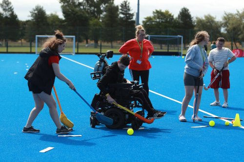 People playing adapted hockey on a blue outdoor pitch, including a participant using a powered wheelchair