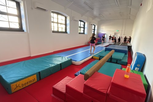 Children using inflatable gymnastics track and balance beam in an indoor training hall.