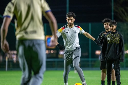 Four men are on a football pitch, one is preparing to kick the ball