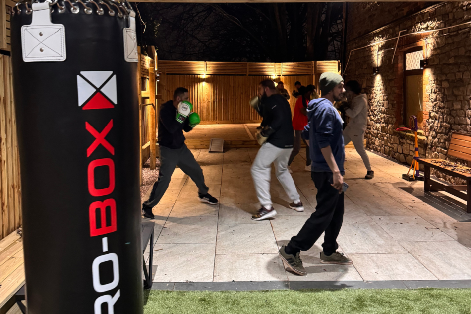  Men sparring alongside a boxing punch bag in an outdoor area.